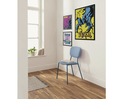 Lichte kamerhoek met drie ingelijste Venom-posters aan de muur, een lichtblauwe stoel met een boek erop en een vloerkleed op de houten vloer.