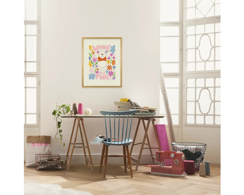 Een lichte ruimte met een bureau, een blauwe stoel, een naaimachine en een Winnie de Poeh poster aan de muur