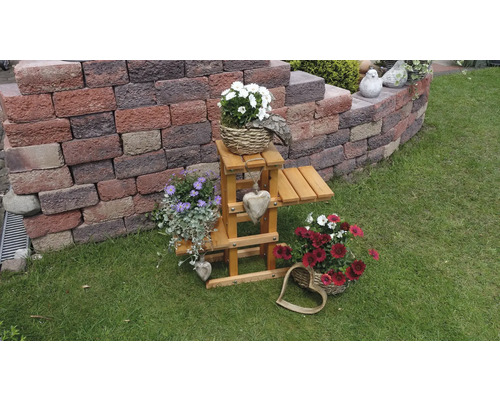 Tuinoverzicht met bloemstukken en houten decoratie op een gazon voor een muur