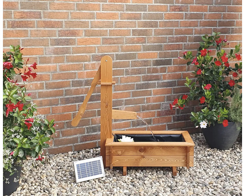 Tuinscene met houten fontein met zonnepomp en plantenbakken voor een bakstenen muur