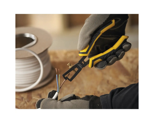 Een persoon gebruikt een draadstripper op een kabel. Op de achtergrond staat een rol kabel.