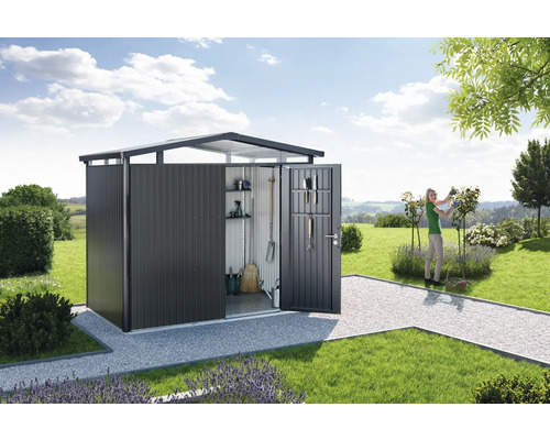 Tuinhuisje met open deur in een tuinlandschap met gazon en een vrouw die rozen snoeit.