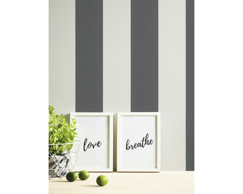 Decoratieve scène met gestreept behang, potplant, twee ingelijste prints met de woorden liefde en ademen, en drie limoenen.