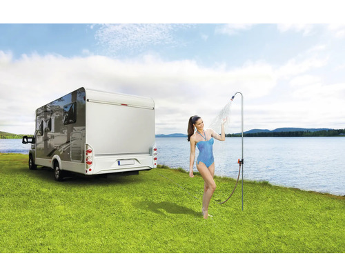 Vrouw onder campingdouche naast camper op gazon aan meer