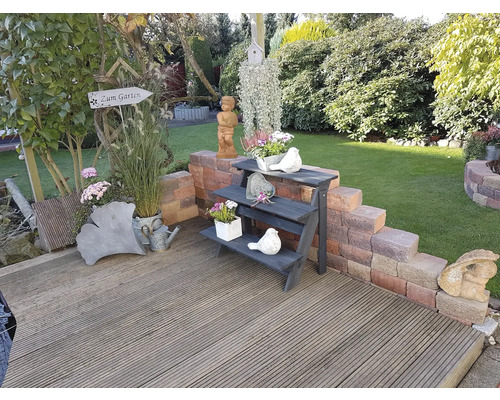 Tuinscène met houten terras, bloemen en decoraties zoals vogeldrinkschaal, figuren en planten