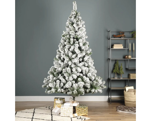 Versierde, besneeuwde kerstboom met geschenken in de woonkamer.