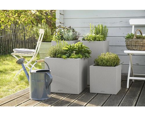 Drie vierkante plantenbakken met kruiden en een gieter in de tuin