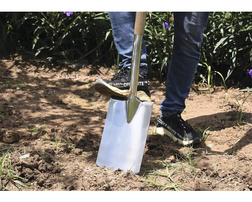Een persoon gebruikt een spade met houten handvat in de tuin om grond uit te graven.