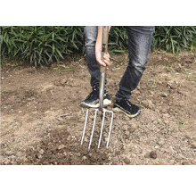 Persoon die een spade met vier tanden in de grond steekt, voor tuinieren