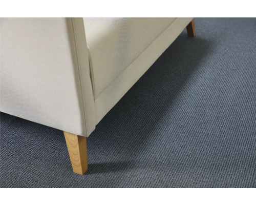 Detail van gestoffeerd meubel met stoffen bekleding en houten poten op een tapijtvloer.