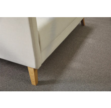 Detailweergave van een gestoffeerde fauteuil met houten poten op een tapijt