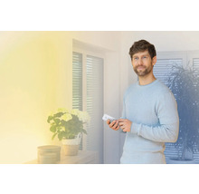 Man bedient met een afstandsbediening een smart home systeem in een lichte woonkamer.