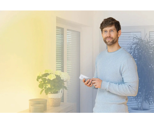 Man bedient met een afstandsbediening een smart home systeem in een lichte woonkamer.