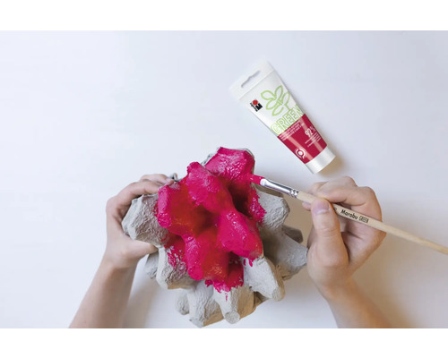 Iemand schildert een eierdoos met een penseel en rode verf, met een tube verf op de achtergrond.