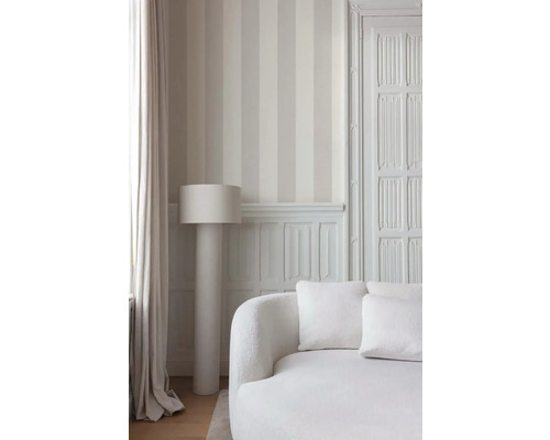 Lichte kamer met gestreept behang, een staande lamp en een sofa.