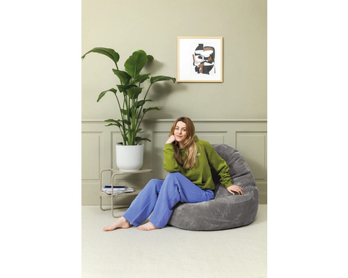 Vrouw zit in een kamer op een grijze zitzak naast een kamerplant en een bijzettafel