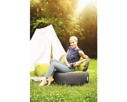 Vrouw zit op een zitzakstoel buiten voor een tent.