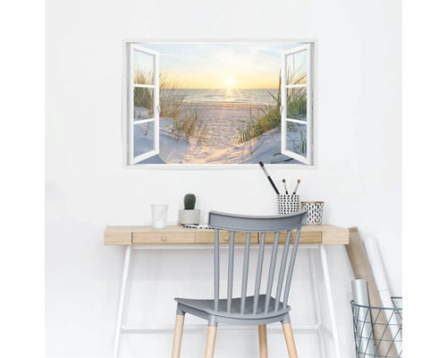Muursticker met uitzicht vanuit het raam op een strand, bureau met kantoorbenodigdheden en stoel op de voorgrond