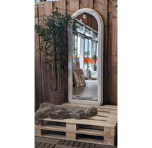 Decoratieve scène met een spiegel met boogframe, een kunstplant en een schapenvacht op een houten pallet