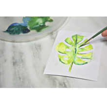 Aquarelschilderij van een Monstera blad met penseel en verfpalet