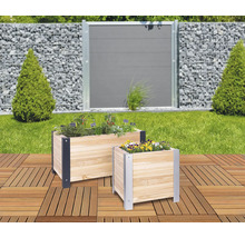 Twee houten plantenbakken met kruiden en bloemen op een terras, met een tuin en hek op de achtergrond.