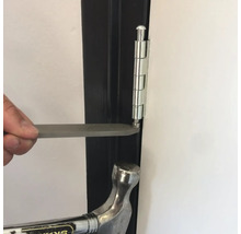 Een man verwijdert met een hamer en een stuk gereedschap een pen uit een deurscharnier.