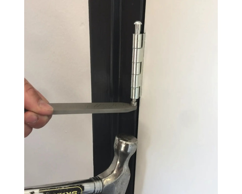 Een man verwijdert met een hamer en een stuk gereedschap een pen uit een deurscharnier.