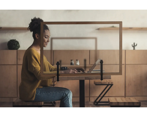 Vrouw werkt op laptop achter een tafelhygiënische bescherming