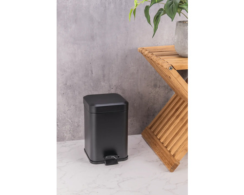 Zwarte metalen pedaalemmer naast een houten kruk met plant