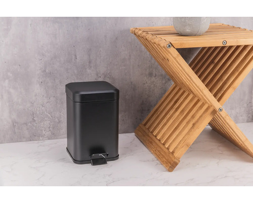 Zwarte metalen pedaalemmer naast een houten krukje.