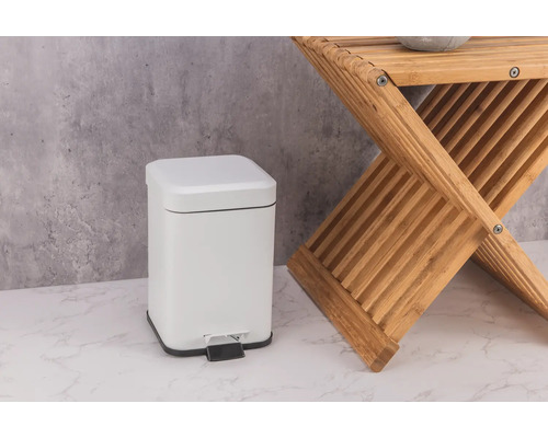 Witte metalen pedaalemmer naast een houten kruk