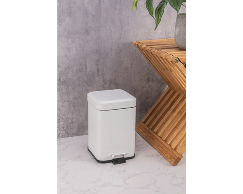 Witte metalen pedaalemmer naast een houten bijzettafel