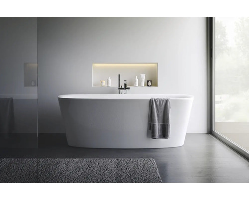 Moderne badkamer met vrijstaand bad, kraan en verzorgingsproducten in een nis.