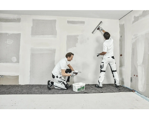 Twee vakmensen stucen een muur in een kamer.