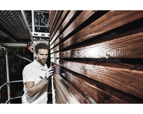 Man schildert houten gevel met kwast en houtbeschermingsglazuur vanaf een steiger