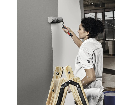 Vrouw schildert muur met verfroller staand op een ladder