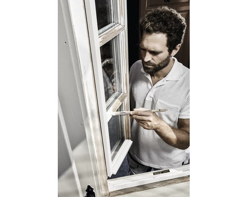 Een man schildert een raam wit met een penseel.