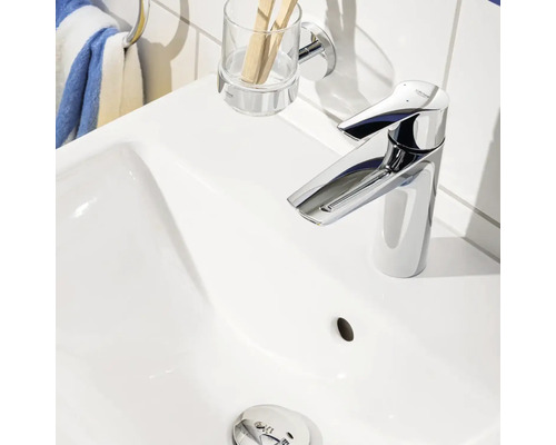 Foto van een witte wastafel met een glanzende kraan, een beker voor tandenborstels en een handdoekhouder