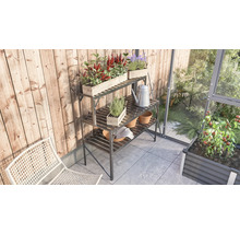 Tuinscene met metalen plantentafel met drie niveaus, beplant met kruiden en bloemen, gieter en tuinhandschoenen