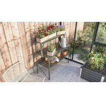Tuinscene met een metalen plantentafel, beplante houten bakken, een gieter en tuingereedschap in een kas