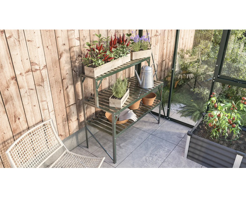 Tuinscene met een metalen plantentafel, beplante houten bakken, een gieter en tuingereedschap in een kas