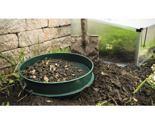 Tuinzeef met aarde, schep en kas op de achtergrond