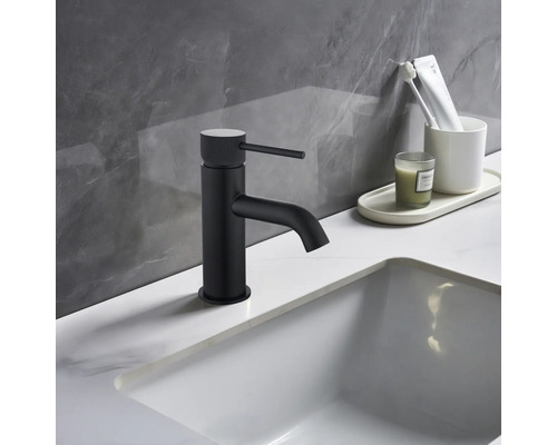 Zwarte wastafelmengkraan naast witte wastafel en badkamerbenodigdheden