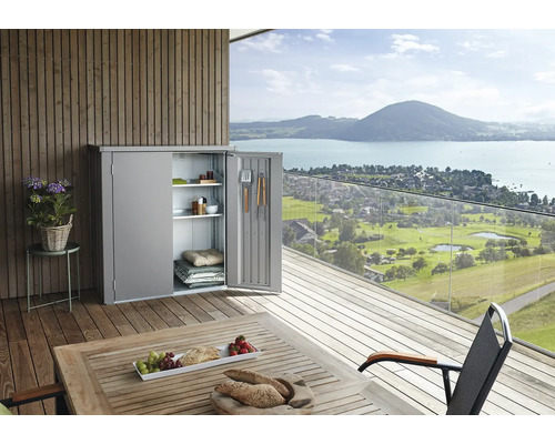 Metalen tuinkast met open deur op een terras met uitzicht op een meer en bergen