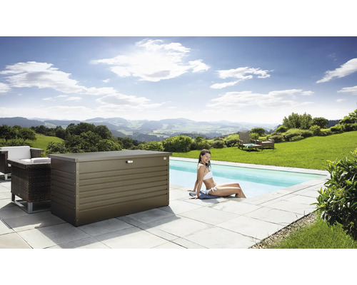 Scene met een metalen opbergbox naast een zwembad, omringd door tuinmeubilair en een vrouw die in het water zit.