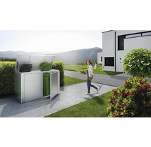Metalen afvalcontainerbox met twee vuilnisbakken en een vrouw met een hark in de tuin