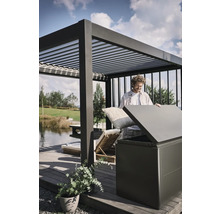 Man stopt kussens in een opbergbox buiten onder een pergola.