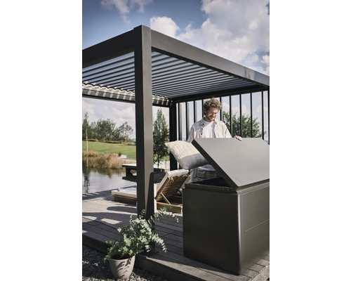 Man stopt kussens in een opbergbox buiten onder een pergola.