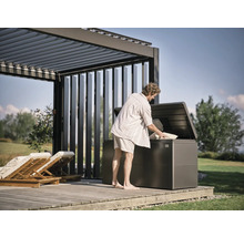 Man vult een tuinkist onder een pergola op een houten terras met kussens.