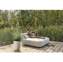 Man ontspant op een tuinligbed met een hoofdtelefoon, naast hem een plantenbak met siergras op een houten terras.